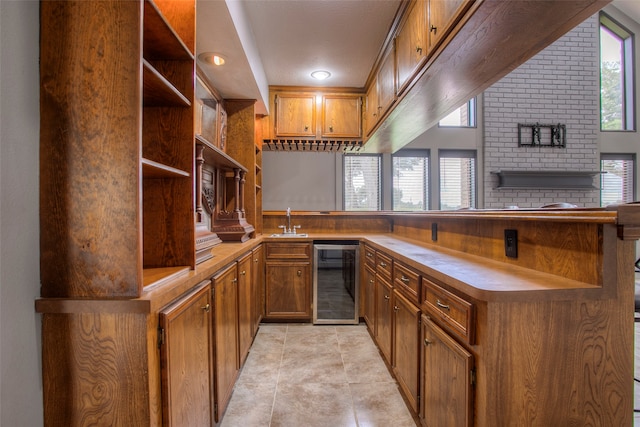 kitchen with kitchen peninsula, light tile patterned flooring, wine cooler, and sink