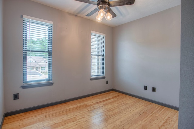 unfurnished room with ceiling fan, wood finished floors, a wealth of natural light, and baseboards