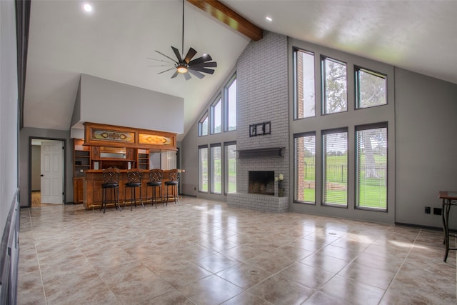 unfurnished living room with ceiling fan, beam ceiling, high vaulted ceiling, and a brick fireplace