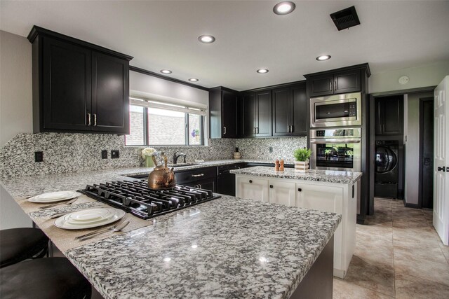 kitchen with a center island, stainless steel appliances, tasteful backsplash, light stone counters, and washer / dryer