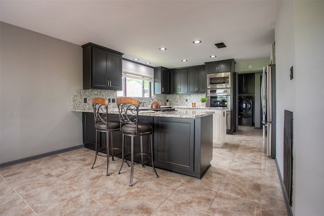 kitchen featuring light stone countertops, stainless steel appliances, kitchen peninsula, decorative backsplash, and a breakfast bar