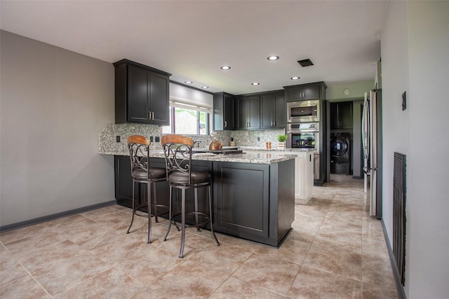 kitchen featuring light stone counters, backsplash, appliances with stainless steel finishes, washer / dryer, and a peninsula