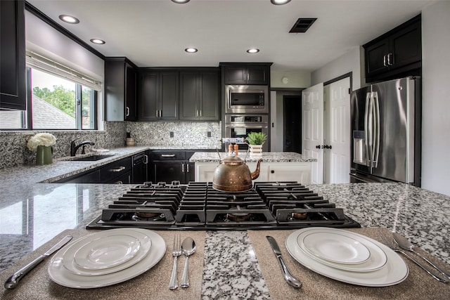 kitchen with backsplash, light stone counters, sink, and appliances with stainless steel finishes