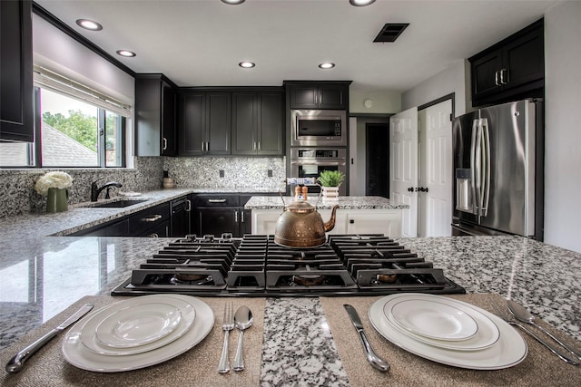 kitchen with tasteful backsplash, visible vents, appliances with stainless steel finishes, dark cabinets, and a sink