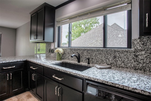 kitchen with light stone counters, a sink, dark cabinetry, decorative backsplash, and dishwasher