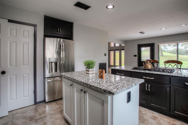 kitchen with gas cooktop, a kitchen island, dark cabinetry, stainless steel refrigerator with ice dispenser, and light stone countertops