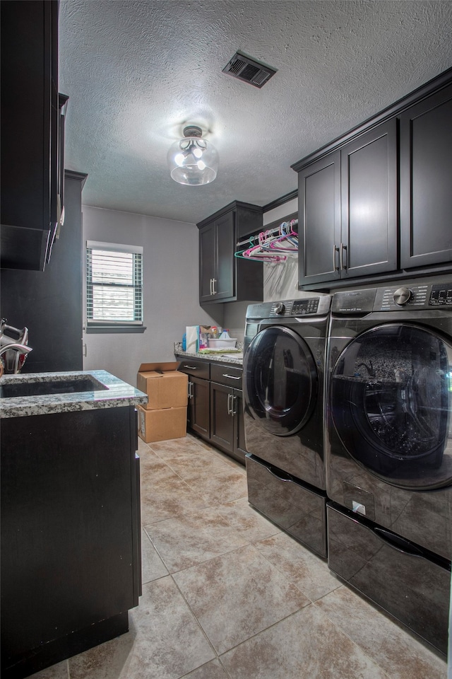 laundry room with washing machine and clothes dryer, light tile patterned floors, cabinets, and a textured ceiling