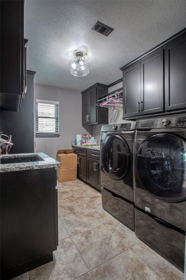 washroom featuring cabinet space, visible vents, a textured ceiling, washing machine and dryer, and a sink