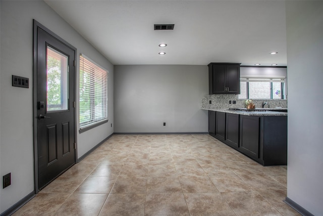 kitchen featuring decorative backsplash, a wealth of natural light, light tile patterned flooring, and light stone countertops