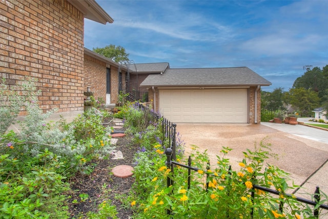 view of home's exterior with a garage, concrete driveway, brick siding, and roof with shingles