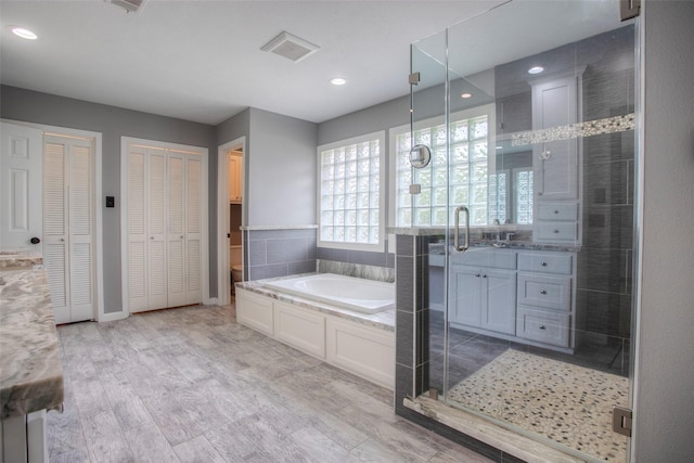 bathroom with wood finished floors, a garden tub, vanity, a shower stall, and a closet