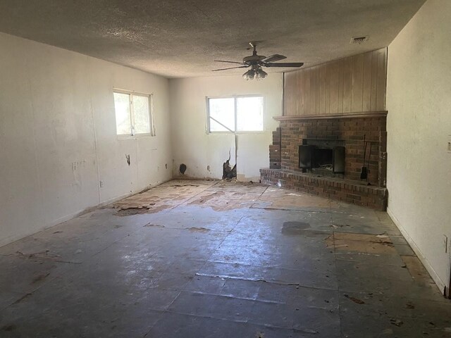 unfurnished living room with a ceiling fan, visible vents, a textured ceiling, and a brick fireplace