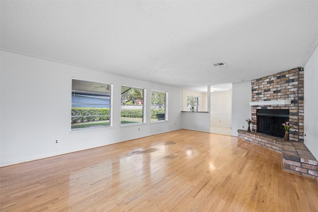 unfurnished living room featuring light hardwood / wood-style floors, a brick fireplace, and a textured ceiling