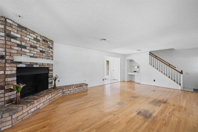 unfurnished living room with a brick fireplace, built in features, a textured ceiling, and light hardwood / wood-style flooring