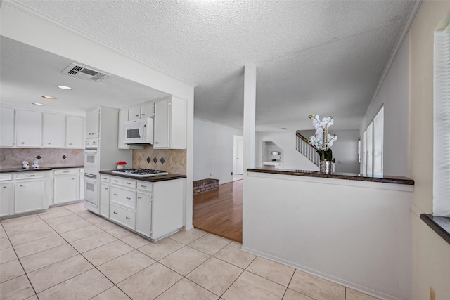 kitchen featuring white cabinetry, light tile patterned floors, kitchen peninsula, white appliances, and decorative backsplash