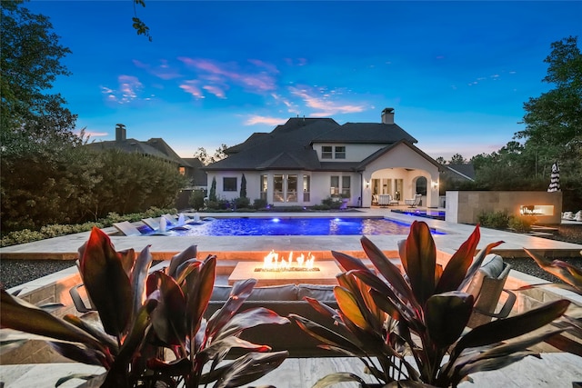 pool at dusk featuring a fire pit, a patio area, and pool water feature