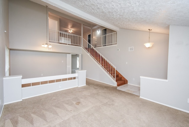 empty room with light colored carpet, a textured ceiling, a chandelier, and a high ceiling