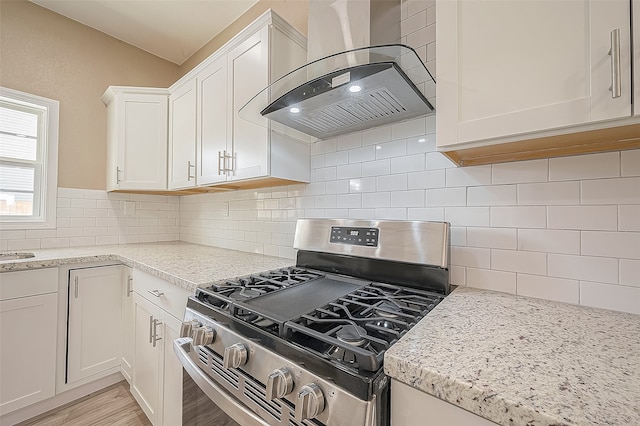 kitchen featuring tasteful backsplash, stainless steel gas range, white cabinets, wall chimney exhaust hood, and light hardwood / wood-style flooring