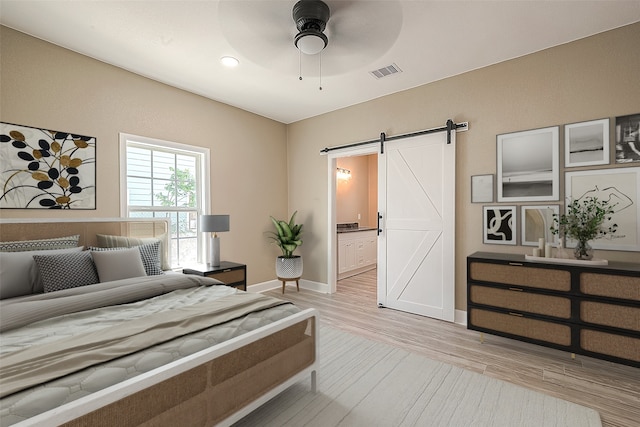 bedroom with light hardwood / wood-style floors, ceiling fan, ensuite bathroom, and a barn door