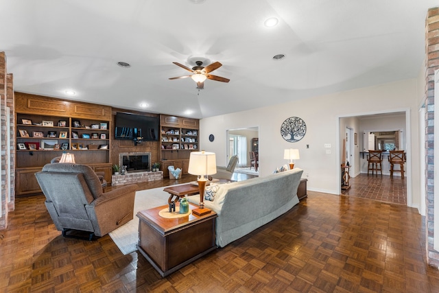 living room with built in features, a fireplace, dark parquet flooring, and ceiling fan