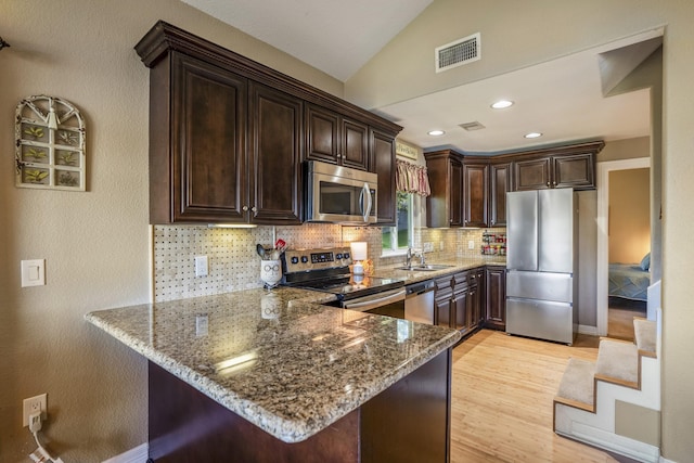 kitchen with dark brown cabinetry, stone counters, stainless steel appliances, and vaulted ceiling