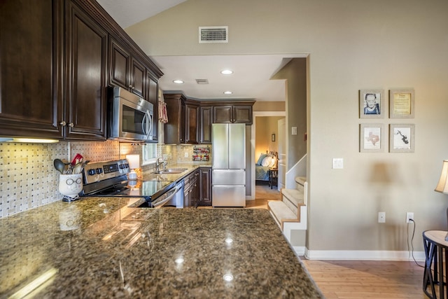 kitchen featuring appliances with stainless steel finishes, dark brown cabinetry, dark stone counters, and backsplash