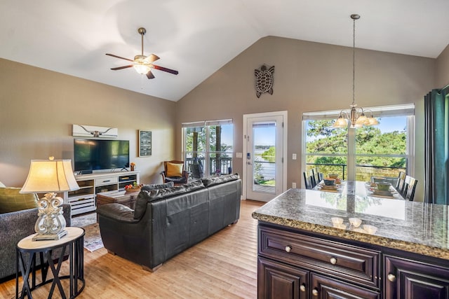 living room with light wood-type flooring, ceiling fan with notable chandelier, and high vaulted ceiling