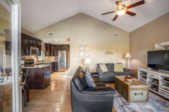 living room with light hardwood / wood-style floors, high vaulted ceiling, and ceiling fan