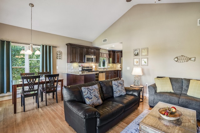 living room featuring a chandelier, light hardwood / wood-style floors, and high vaulted ceiling