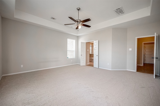 unfurnished bedroom with a tray ceiling, light colored carpet, and ensuite bathroom