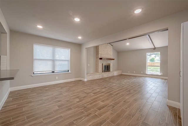 unfurnished living room featuring vaulted ceiling, light hardwood / wood-style flooring, and a brick fireplace