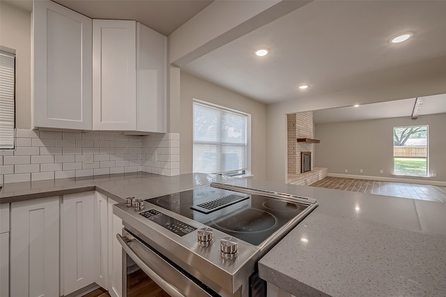 kitchen with stainless steel electric stove, tasteful backsplash, white cabinets, light stone countertops, and hardwood / wood-style flooring