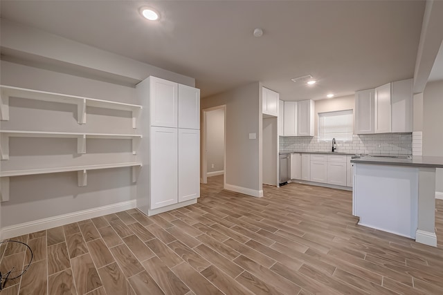 kitchen with white cabinets, sink, kitchen peninsula, stainless steel dishwasher, and light hardwood / wood-style flooring