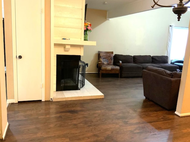 living room with a tiled fireplace, ceiling fan, and dark wood-type flooring