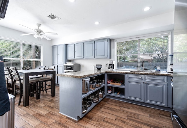 kitchen featuring dark hardwood / wood-style floors, sink, kitchen peninsula, dark stone countertops, and ceiling fan