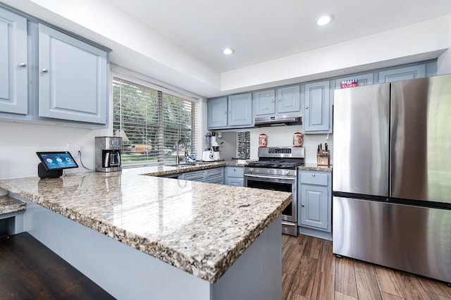 kitchen with light stone counters, sink, kitchen peninsula, appliances with stainless steel finishes, and dark hardwood / wood-style flooring