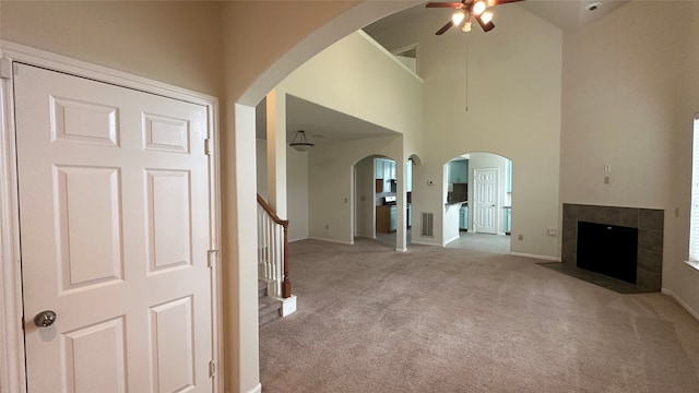 unfurnished living room featuring ceiling fan, a tiled fireplace, a high ceiling, and light carpet