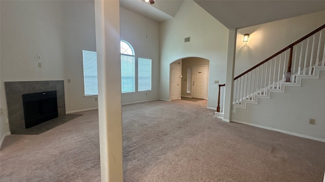 unfurnished living room with light carpet, high vaulted ceiling, and a tile fireplace