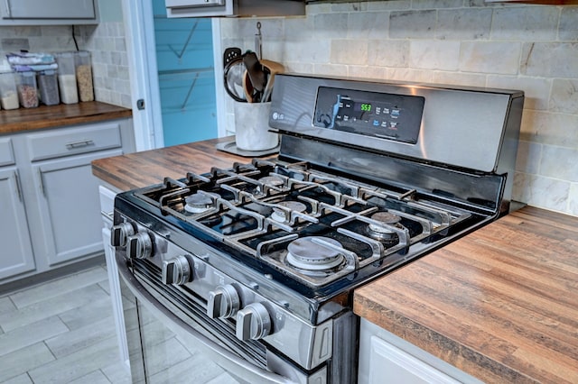 room details with decorative backsplash, gray cabinetry, butcher block counters, and black range with gas cooktop