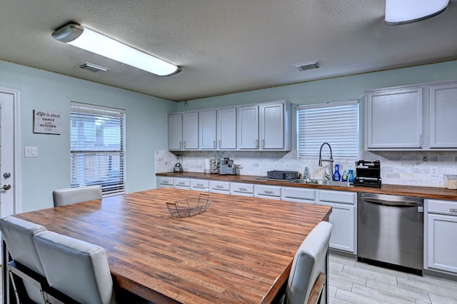 kitchen with tasteful backsplash, sink, white cabinetry, butcher block counters, and stainless steel dishwasher