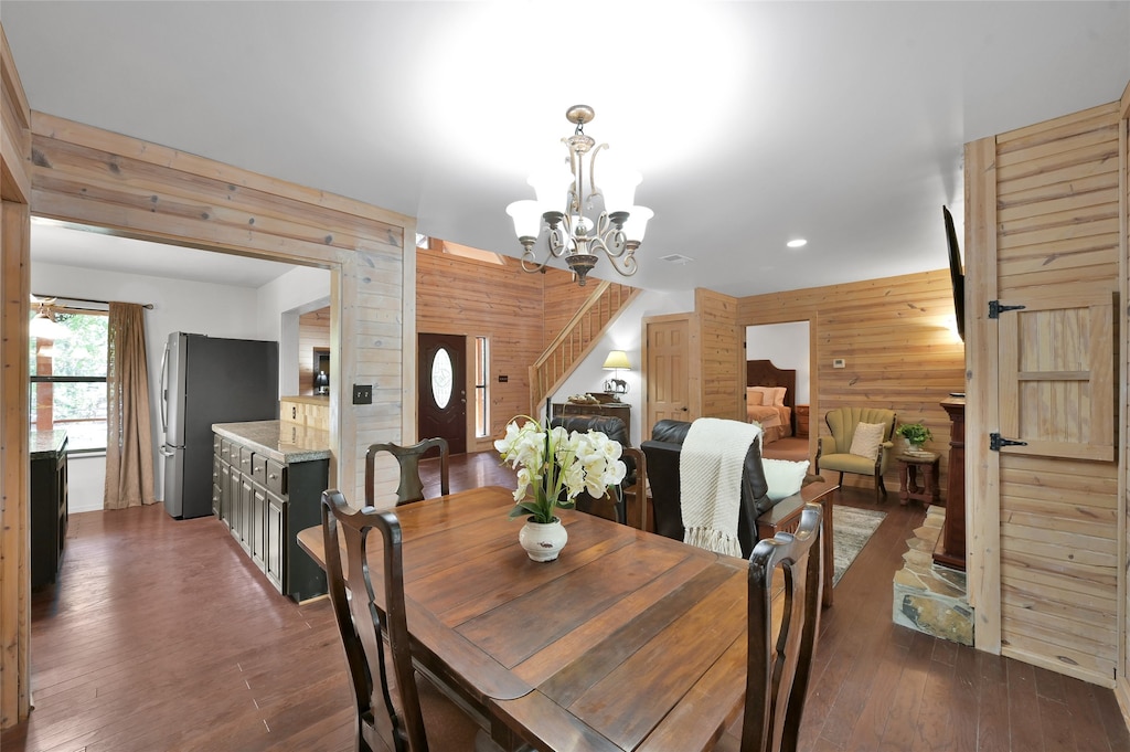 dining space featuring wooden walls, dark hardwood / wood-style floors, and an inviting chandelier