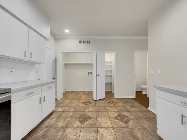 kitchen with stainless steel stove, white cabinets, backsplash, and crown molding