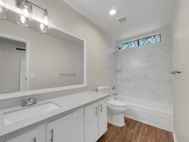 full bathroom with hardwood / wood-style floors, vanity, tiled shower / bath combo, and toilet