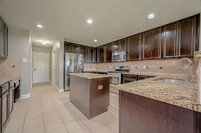 kitchen with tasteful backsplash, stainless steel appliances, a textured ceiling, a center island, and sink