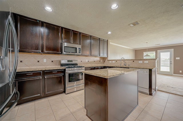 kitchen featuring appliances with stainless steel finishes, crown molding, a kitchen island, and decorative light fixtures