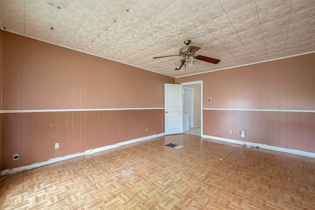 empty room featuring light parquet floors, wood walls, and ceiling fan