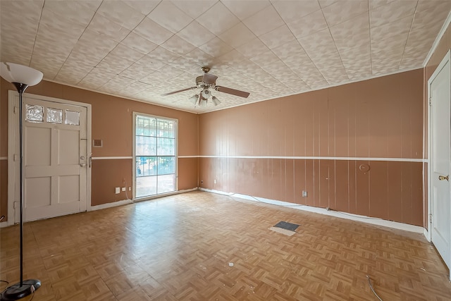 interior space featuring wooden walls, ceiling fan, and light parquet floors