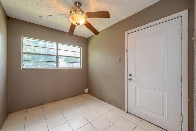 empty room with a textured ceiling, light tile patterned floors, and ceiling fan