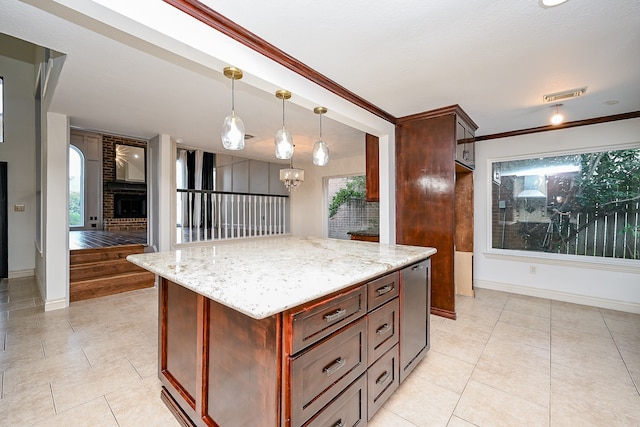 kitchen featuring hanging light fixtures, a fireplace, a kitchen island, light stone countertops, and crown molding