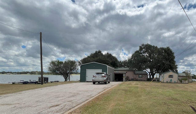 view of front of home featuring a garage, a water view, a front lawn, and an outbuilding